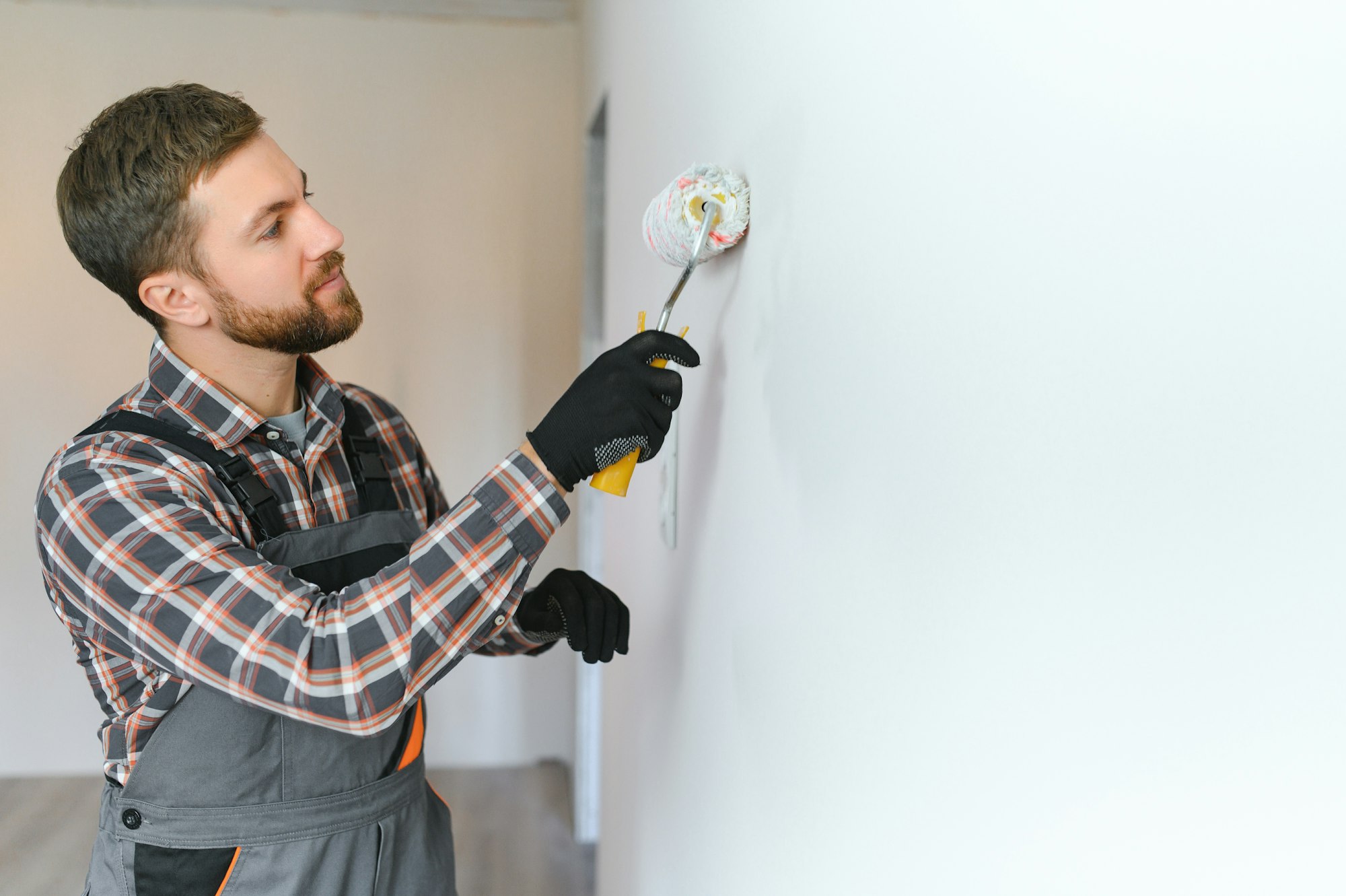 Painter painting a wall with paint roller. Builder worker painting surface with white color